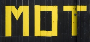 MOT crudely painted in yellow on black wooden background