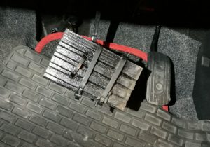 A brake pedal with a section of wooden decking affixed to it with black cable ties.